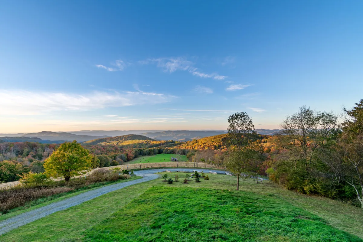 A sweeping view of rolling hills and distant mountains under a clear blue sky, dotted with colorful foliage. The foreground hints at hiking trails and open spaces perfect for outdoor activities like photography and nature watching. The serene ambiance captures the essence of mountain exploration and the grandeur of the surrounding landscape.