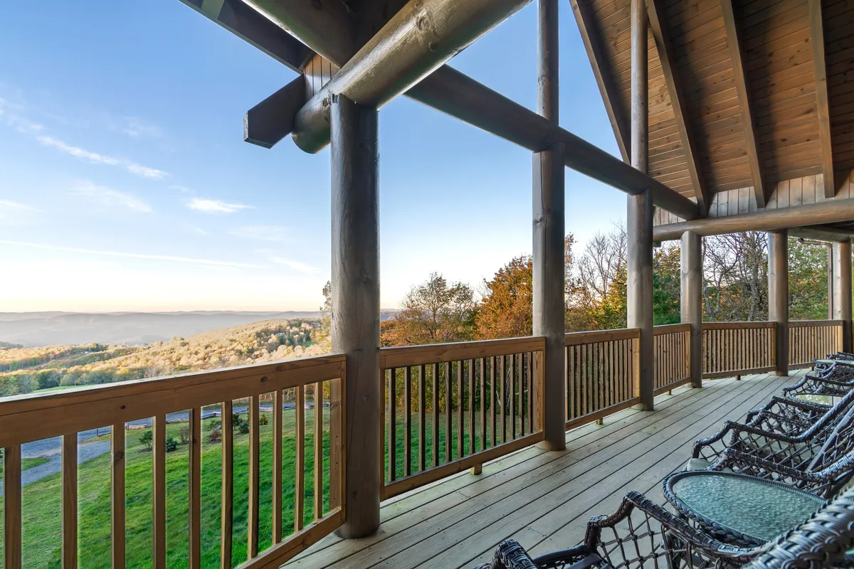 A covered deck with wooden railings, several rocking chairs, and a breathtaking mountain view stretching into the distance. The space is ideal for outdoor meals or soaking up the scenery with friends and family.