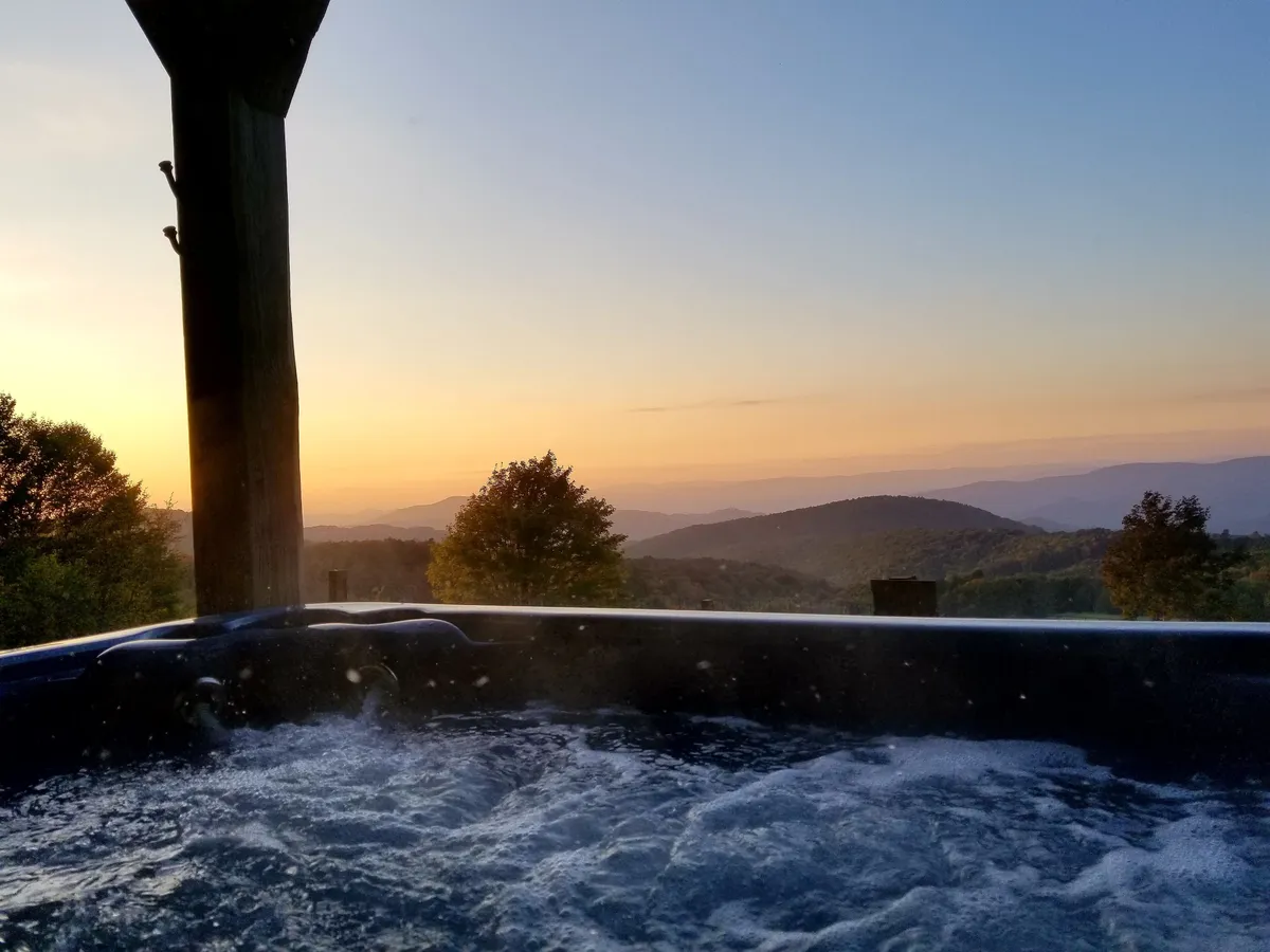 An outdoor hot tub overlooking a stunning mountain view at sunset. The bubbling water and serene woodland surroundings create an atmosphere ideal for relaxation and stargazing.