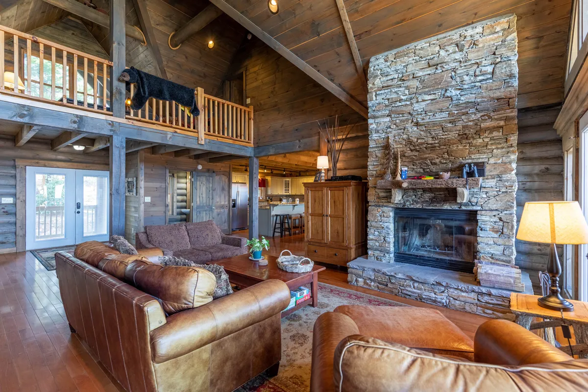 A cozy interior scene centered on a stone fireplace and leather sofa, with rustic wooden beams and a balcony featuring a black bear rug. The inviting space is perfect for relaxing with your dog after outdoor activities.