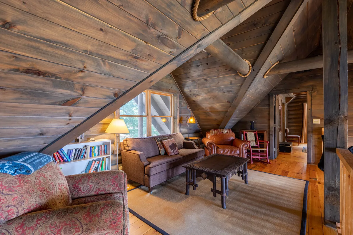 An airy loft lounge with exposed wooden beams, large windows, plush seating, and a bookshelf. The space is flooded with natural light, offering sweeping mountain views and a perfect nook for curling up with a book or enjoying tranquil solitude.