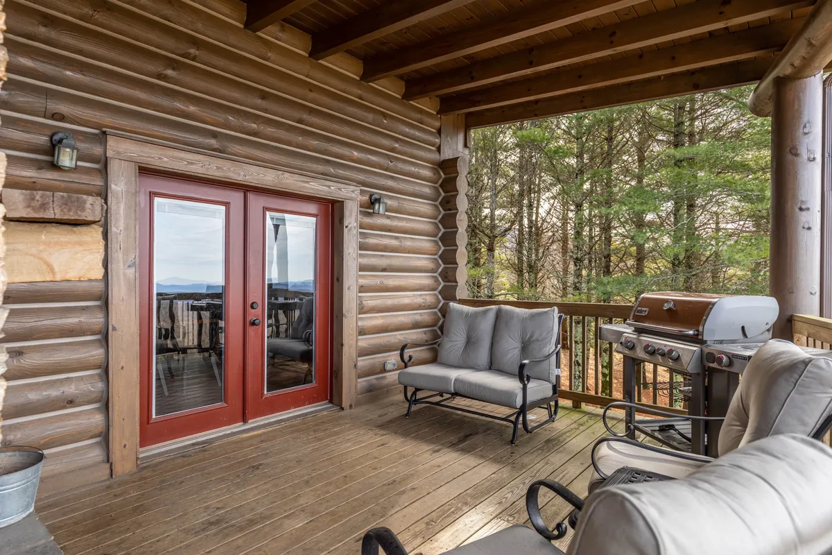 A stylish exterior deck setup with French doors opening onto a comfortable seating area and a modern grill. The deck overlooks a beautiful natural setting, making it ideal for al fresco dining, barbecues, and relaxed lounging.