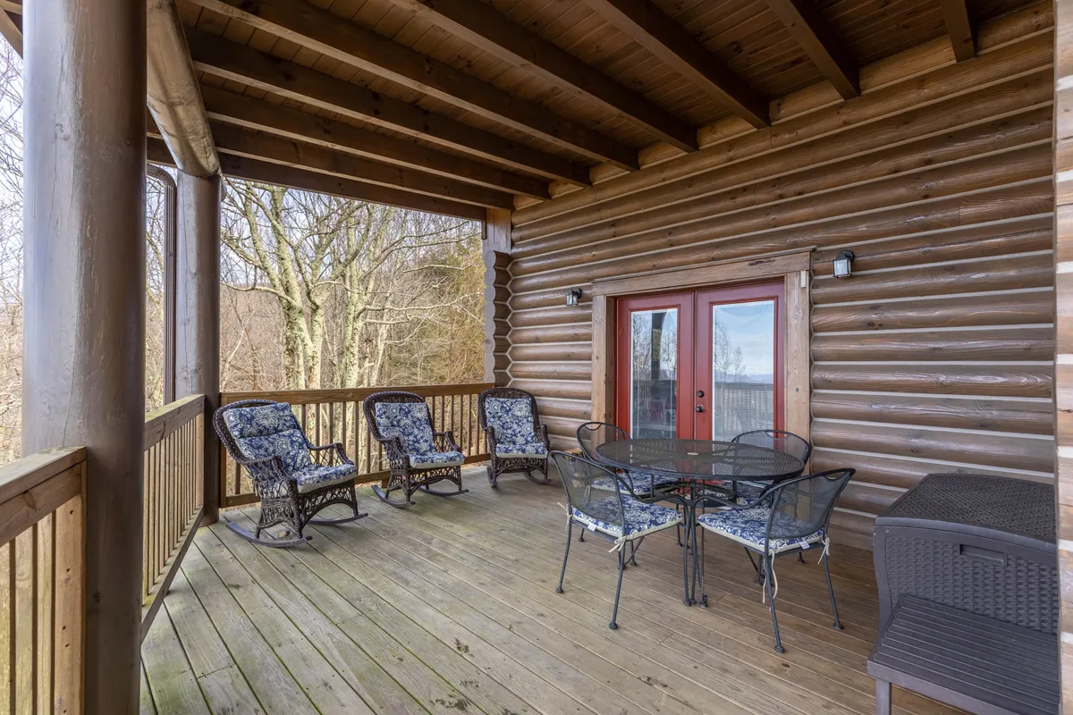 A welcoming front porch with red double doors, wicker chairs, and a glass-top table, set against the backdrop of wooden log walls. The area is ideal for relaxing with a book, enjoying coffee, or gathering with friends while being immersed in the outdoors.