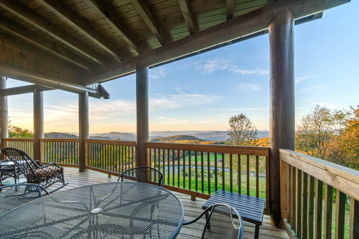 An outdoor seating area overlooking sweeping mountain views, with sturdy wooden beams framing the space. The seating invites guests to relax, dine, or socialize while soaking in the mountain vistas and the changing colors of the sky at sunset.