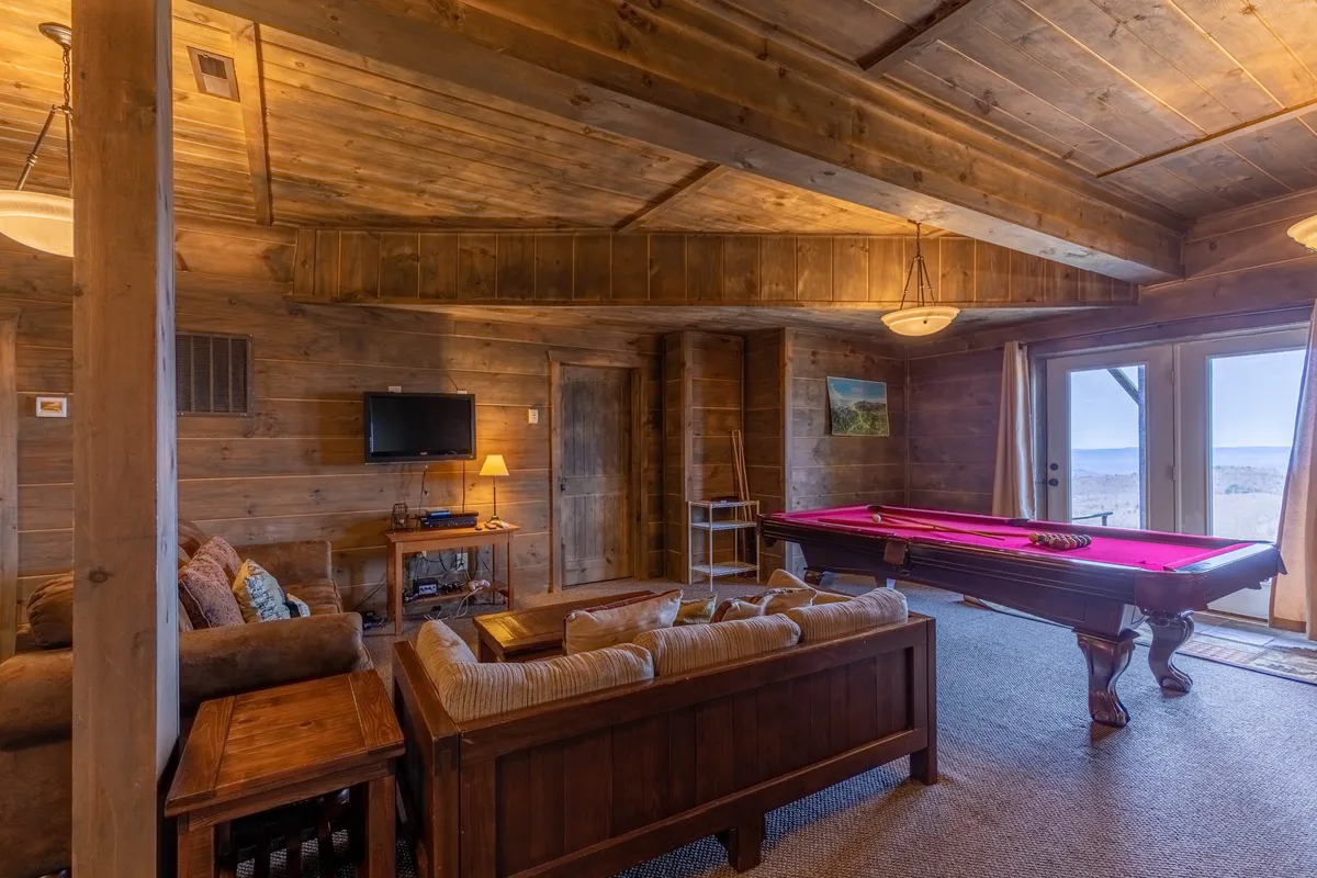 An inviting interior space with a pool table, sofa, TV, and broad windows providing scenic views. The seating area is perfect for both watching movies or sports and relaxing after a game.