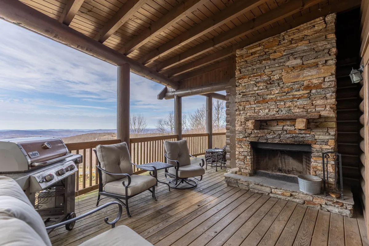 A spacious outdoor deck featuring a large stone fireplace, comfortable seating areas, and a modern grill. The deck opens to sweeping mountain views, inviting both relaxation and social gatherings. The warm glow of the fireplace and open sky create an inviting atmosphere perfect for evening gatherings or quiet mornings.