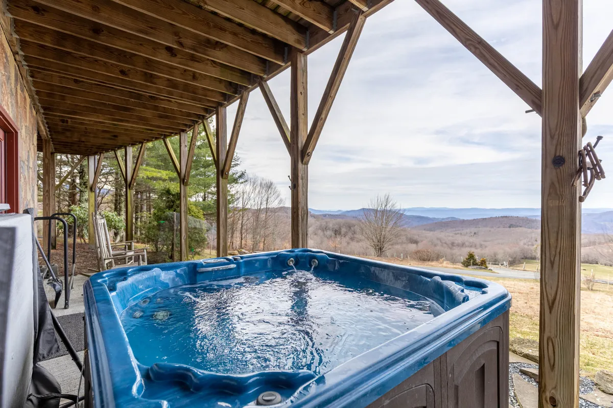 A private hot tub perched on a wooden deck, overlooking a stunning mountain view. The scene is tranquil, inviting guests to relax while taking in the sunrise or gaze at the stars on clear nights. The wooden structure enhances the natural, cozy mountain retreat feel.